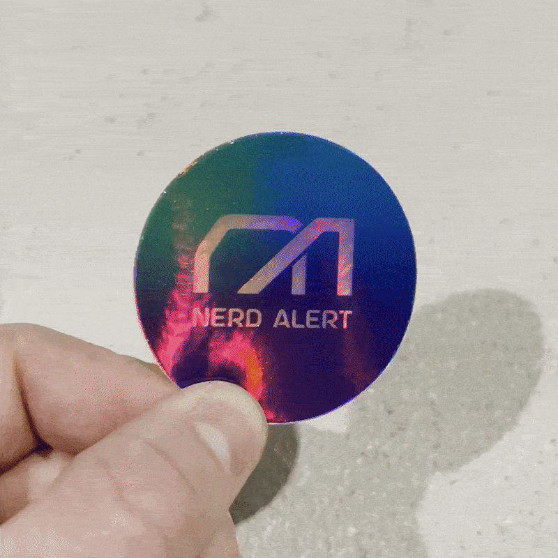 A round rainbow holographic sticker shimmering back and fourth with the Nerd Alert logo as the primary design.